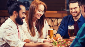 Friends eating around a table glasses food drinks pizza